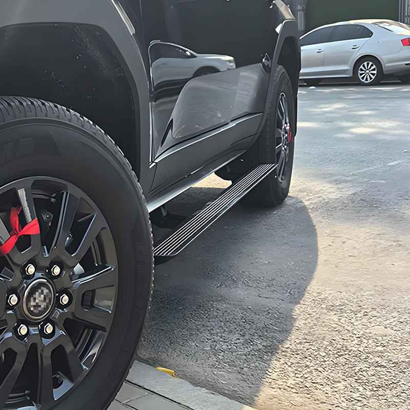 Detailed view of the extended Land Cruiser 250 power running boards on a black SUV, showing the step deployment next to the rugged black alloy wheel.