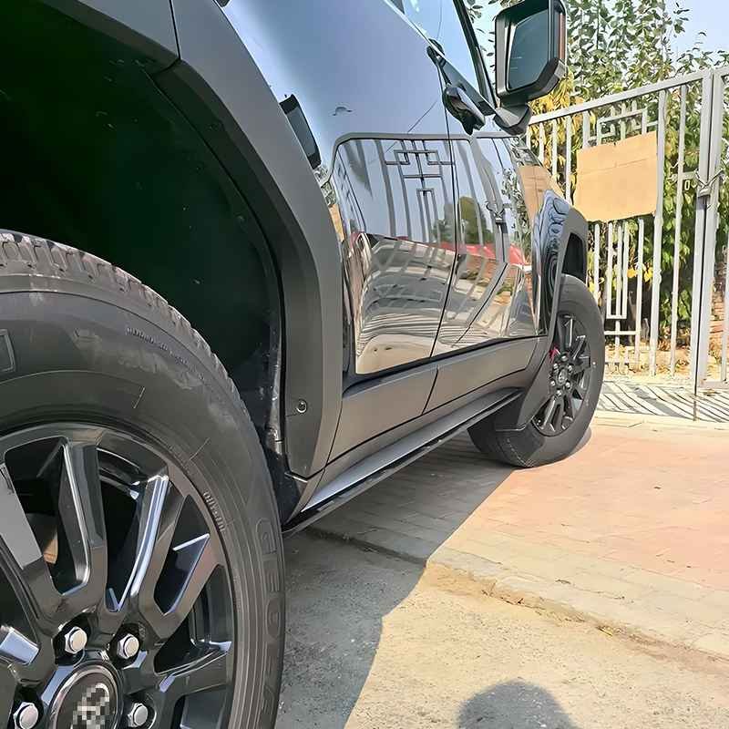 Urban outdoor view of a black Land Cruiser 250 with Land Cruiser 250 power running boards retracted neatly beneath the body, parked next to a metal fence.