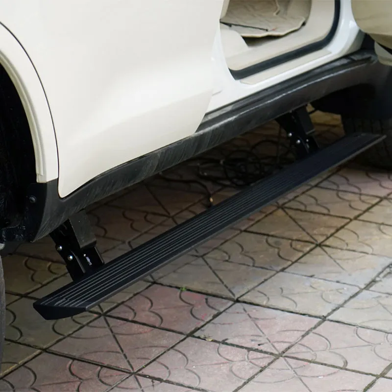 Close-up view of the deployed Toyota FJ power running boards on a white car, highlighting the aluminum textured non-slip surface and the mounting brackets.