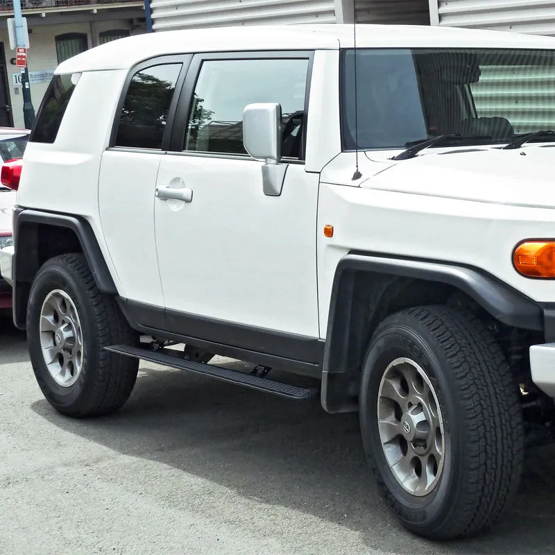 Rear-side view of a white Toyota FJ Cruiser showing the deployed Toyota FJ power running boards positioned under the passenger doors for easy stepping.