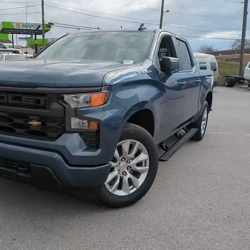 Side profile of a blue pickup truck installed with Chevy Silverado Power Running Boards in a parking lot.