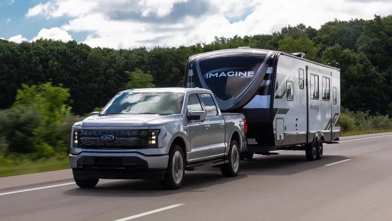 A silver Ford F-150 towing a large Imagine travel trailer down a highway, demonstrating its strong ford f150 towing capacity