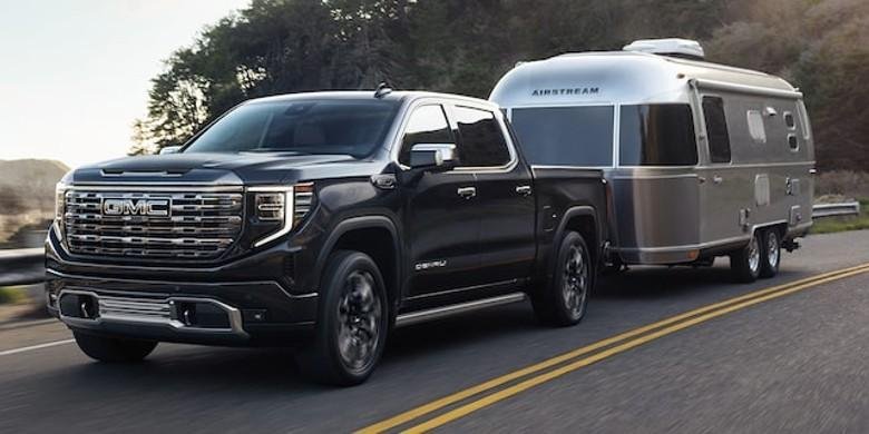 A black GMC Sierra 1500 towing a silver Airstream travel trailer on a scenic road, showcasing its powerful gmc sierra 1500 towing capacity.