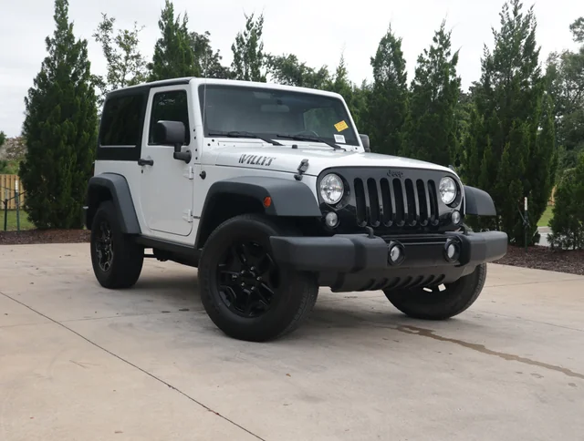 White 2-door Jeep Wrangler Willys with black rims and bumper parked on a driveway, illustrating the durable chassis related to jeep wrangler towing capacity.