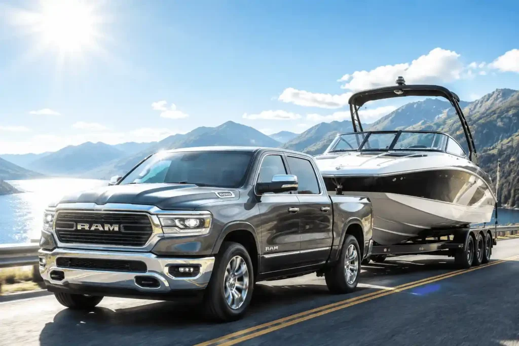 A gray Ram 1500 pickup truck towing a large speedboat on a sunny highway with mountains, showcasing its impressive ram 1500 towing capacity.