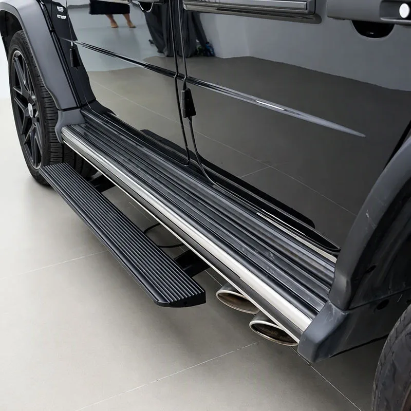 Close-up side profile of a black Mercedes-Benz G500 showing the deployed Mercedes-Benz G500 Electric Running Boards with a textured anti-slip surface above dual side exhausts.