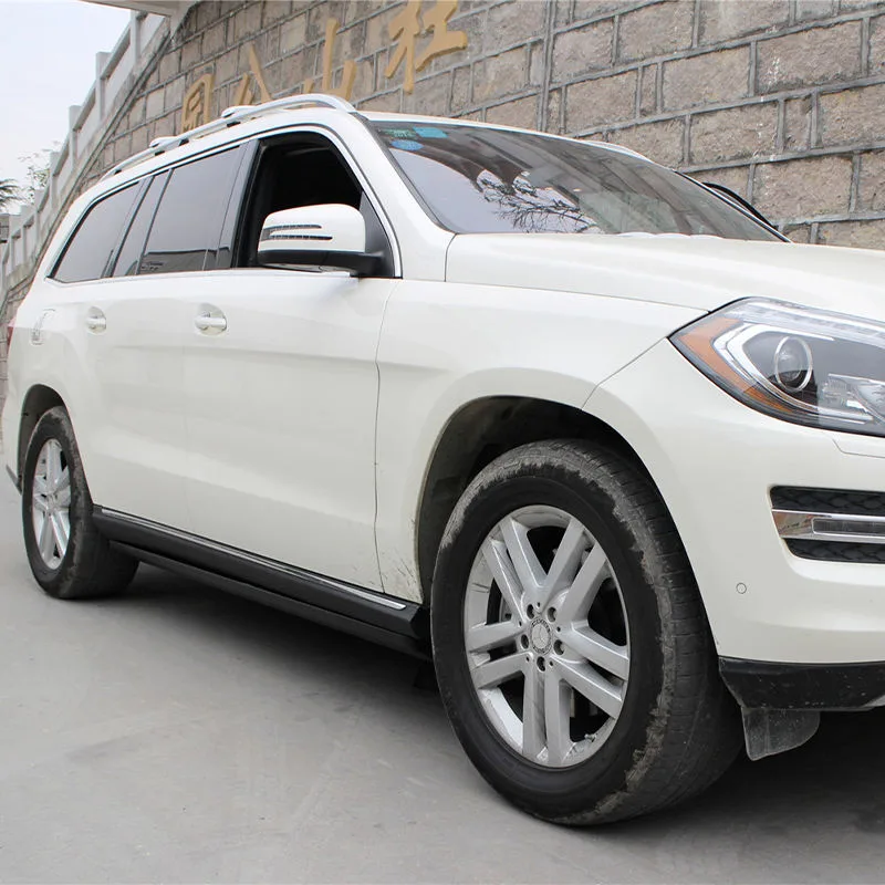 Outdoor front-side view of a white Mercedes-Benz GL SUV equipped with Mercedes-Benz GL Electric Running Boards, shown in the retracted position for a sleek profile.