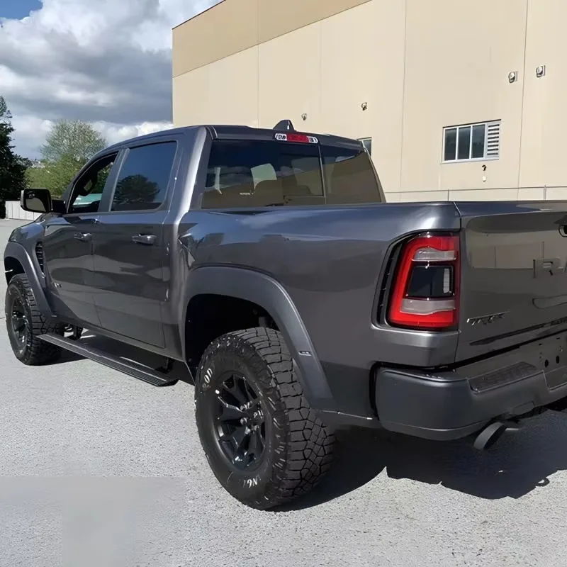Rear-side angle of a dark gray Ram 1500 TRX with electric side steps deployed, highlighting the rear bed, taillights, and flush-mounted running board design.