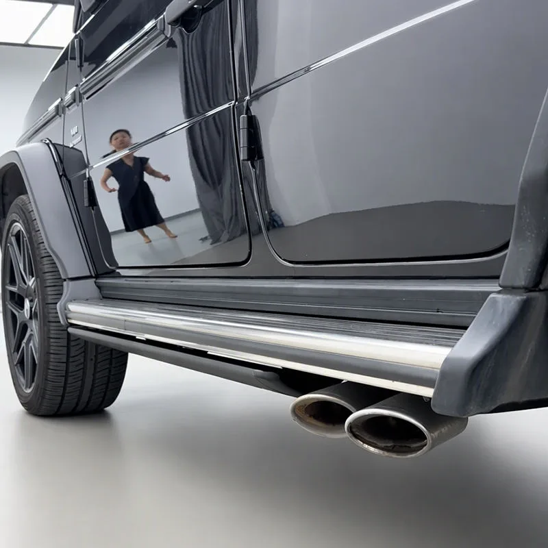 Side profile of a black Mercedes-Benz G500, showing the retracted Mercedes-Benz G500 Electric Running Boards tucked flush against the vehicle's chassis above the dual exhaust tips.