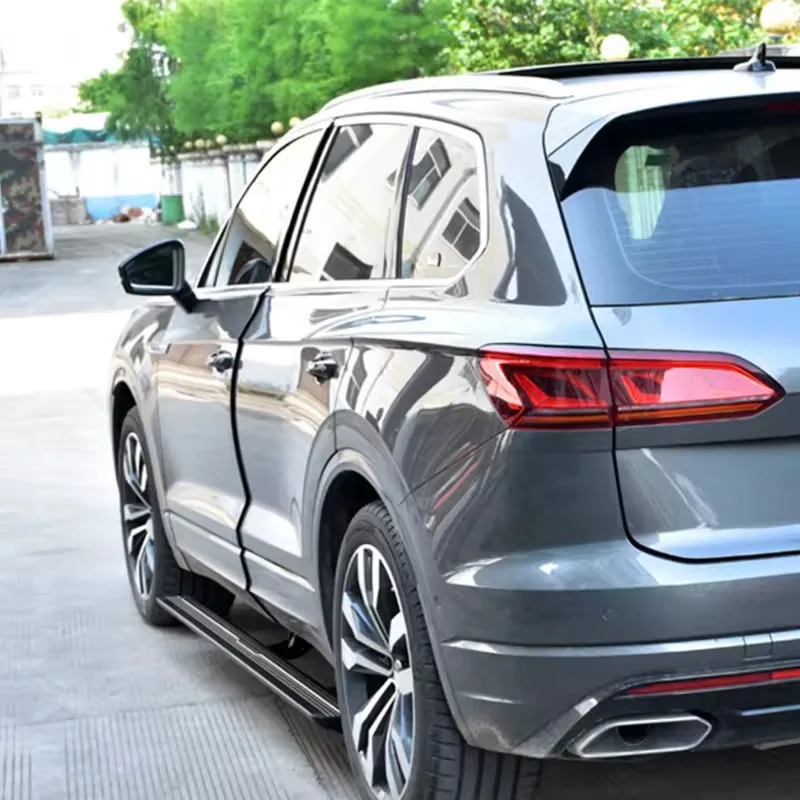 Rear quarter view of a grey Volkswagen Touareg parked outdoors, displaying the Touareg electric side steps mounted underneath the doors.