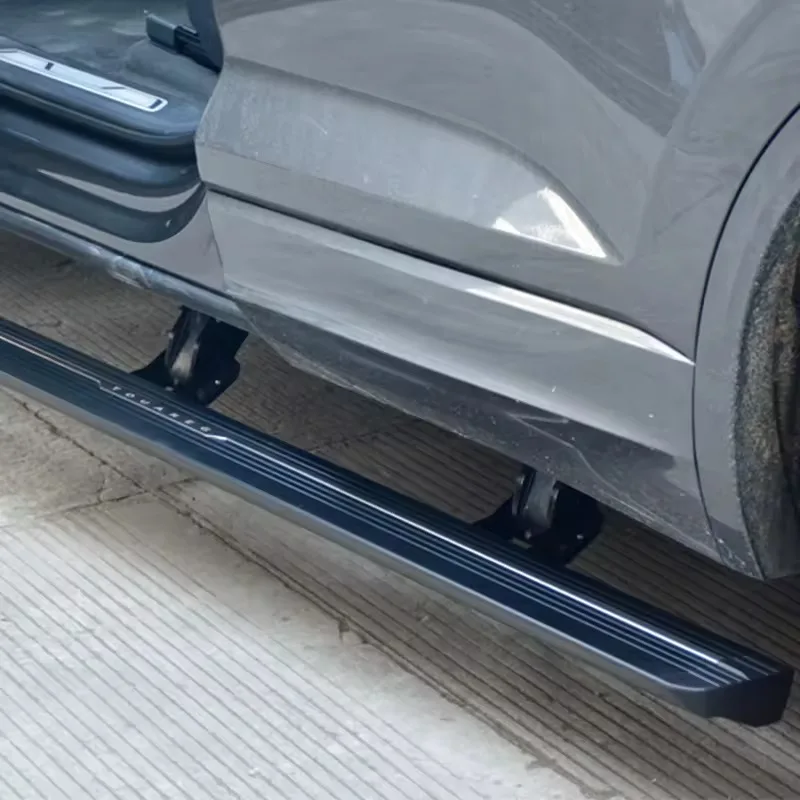Close-up view of a deployed Touareg electric side step on a grey SUV, highlighting the black running board with TOUAREG lettering and the sturdy motorized hinge brackets.