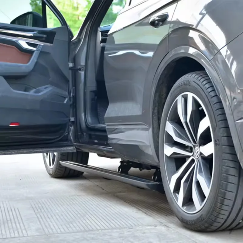 A grey Volkswagen Touareg with the front door open, clearly showing the fully deployed Touareg electric side steps, mounting brackets, and alloy wheel.