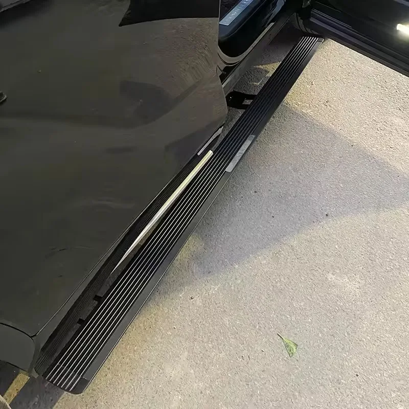 Outdoor close-up of the deployed Land Rover Discovery 5 Electric Side Steps on a black SUV, showing the rugged tread pattern and step access on a sunny day.