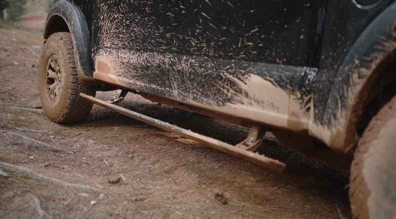 Close-up of a mud-covered electric running board deployed on a dirty off-road SUV.