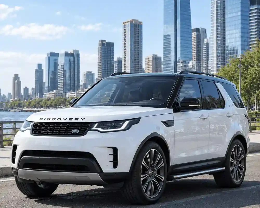 A white Land Rover Discovery SUV parked near a waterfront with a city skyline behind it. The photo showcases its versatile design and is relevant for searches regarding range rover power running boards, which are a popular upgrade for enhancing side-step accessibility on similar Land Rover models.