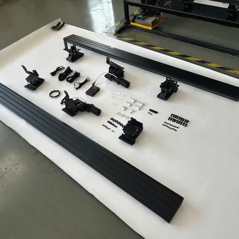 Exploded view of an Electric Running Board Sample kit laid out on a white surface, displaying two black step bars, electric drive motors, mounting brackets, a wiring harness, a control module, and various assembly hardware.