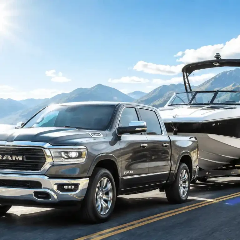 A gray Ram 1500 pickup truck towing a large speedboat on a sunny highway with mountains, showcasing its impressive ram 1500 towing capacity.